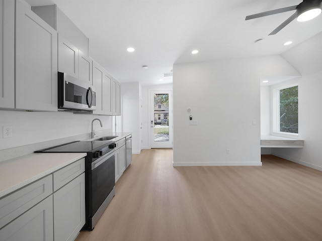 kitchen with light countertops, ceiling fan, stainless steel appliances, light wood finished floors, and a sink