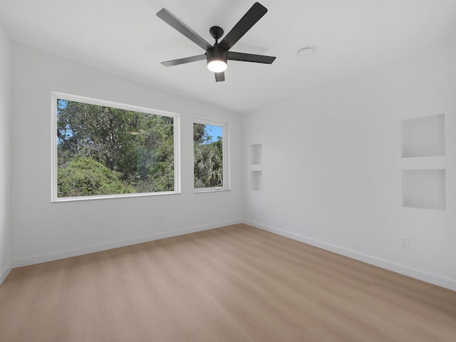 empty room featuring built in features, light wood finished floors, baseboards, and a ceiling fan