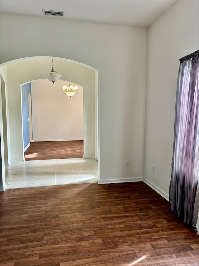 spare room featuring wood finished floors, a notable chandelier, visible vents, and arched walkways