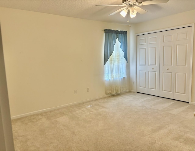 unfurnished bedroom featuring ceiling fan, a closet, light colored carpet, and a textured ceiling