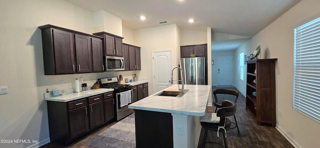 kitchen featuring dark wood-type flooring, sink, an island with sink, a kitchen bar, and stainless steel appliances