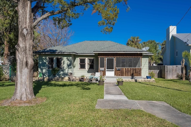 bungalow with a sunroom, a shingled roof, a front yard, and fence