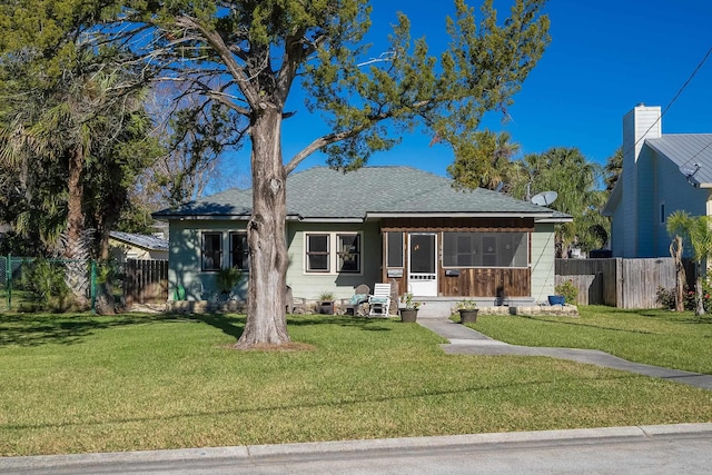 bungalow with a sunroom, roof with shingles, a front yard, and fence