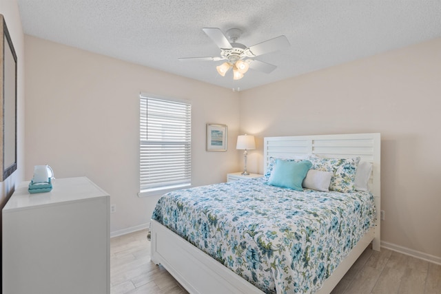 bedroom featuring baseboards, a textured ceiling, light wood-style floors, and a ceiling fan