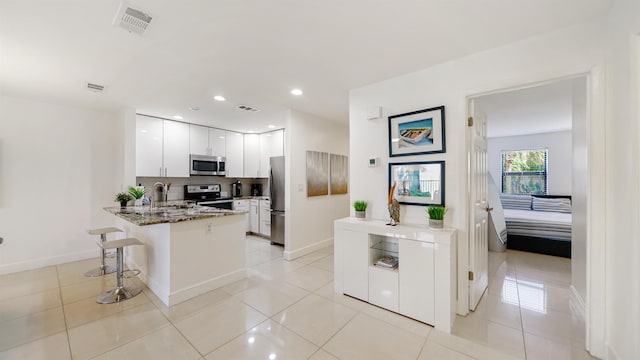 890 A1A Beach Blvd Unit 59, Saint Augustine, FL 32080 - kitchen featuring appliances with stainless steel finishes, a peninsula, white cabinetry, dark stone countertops, and a breakfast bar