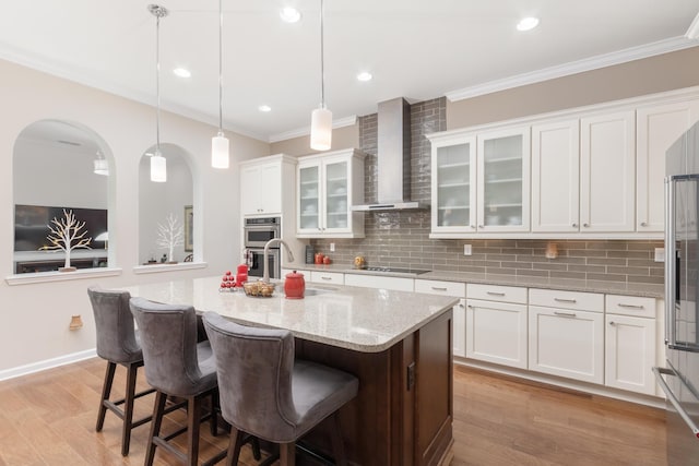 kitchen featuring hanging light fixtures, a center island with sink, white cabinets, and wall chimney exhaust hood