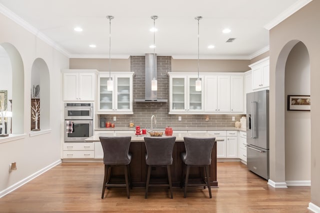 kitchen featuring appliances with stainless steel finishes, a center island with sink, a kitchen bar, decorative light fixtures, and wall chimney exhaust hood