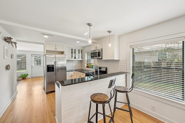 kitchen featuring appliances with stainless steel finishes, white cabinets, hanging light fixtures, light hardwood / wood-style floors, and kitchen peninsula