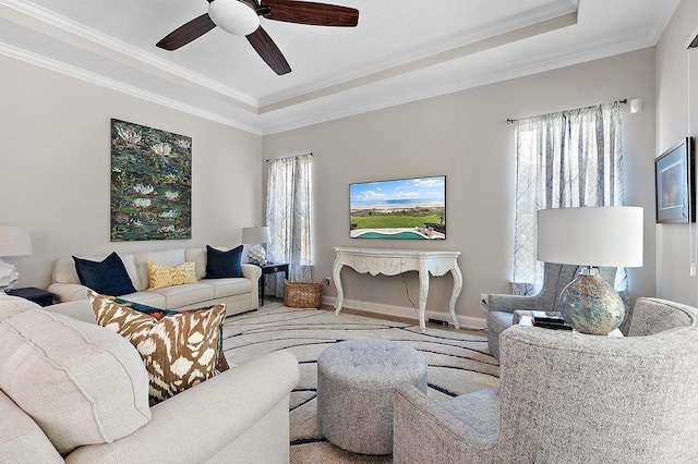 living room with baseboards, a raised ceiling, a ceiling fan, and ornamental molding