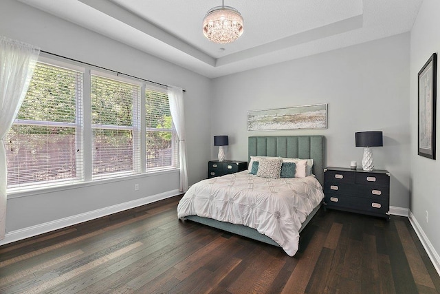 bedroom with hardwood / wood-style floors, a tray ceiling, baseboards, and a chandelier