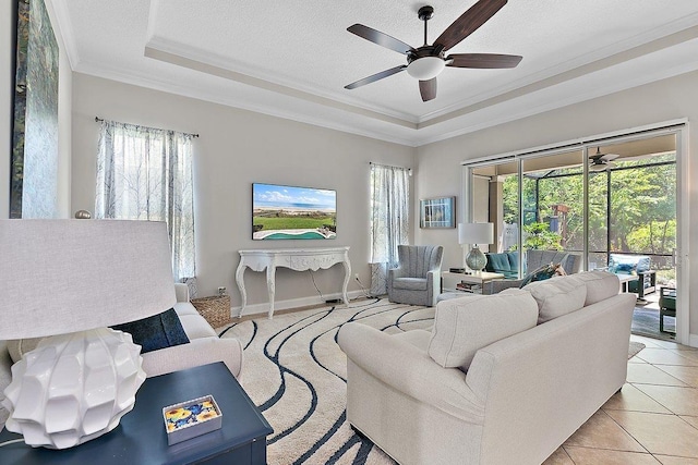 living area featuring ornamental molding, light tile patterned flooring, a textured ceiling, a raised ceiling, and a ceiling fan