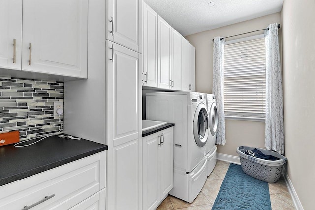 laundry area with baseboards, light tile patterned flooring, cabinet space, a textured ceiling, and washing machine and dryer