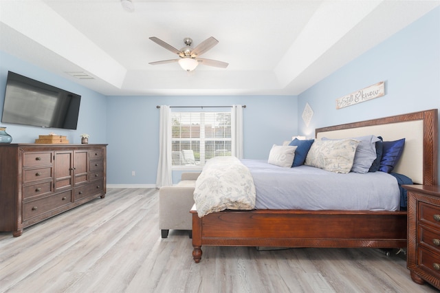 bedroom with baseboards, ceiling fan, a tray ceiling, and light wood-style floors