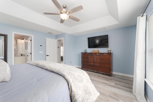 bedroom with light wood-style floors, baseboards, a raised ceiling, and a ceiling fan