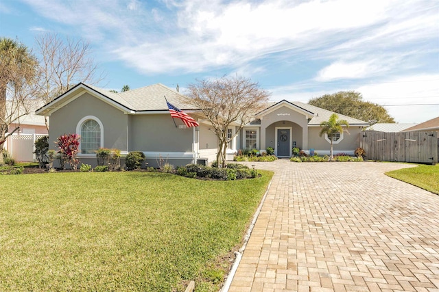 ranch-style home featuring a front yard, fence, decorative driveway, and stucco siding