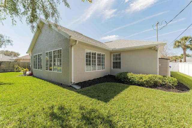 view of home's exterior with roof with shingles, a lawn, fence, and stucco siding