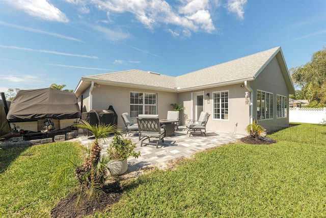 rear view of property with roof with shingles, stucco siding, a lawn, a patio area, and fence