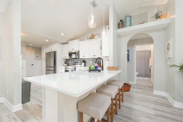 kitchen with a breakfast bar, arched walkways, light countertops, backsplash, and appliances with stainless steel finishes