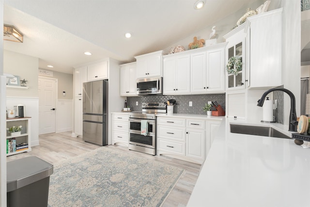 kitchen featuring light wood-style flooring, stainless steel appliances, a sink, white cabinets, and light countertops