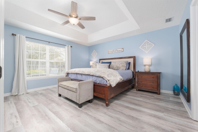 bedroom featuring a tray ceiling, visible vents, baseboards, and wood finished floors