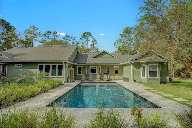 rear view of house featuring a patio, roof with shingles, a lawn, and an outdoor pool