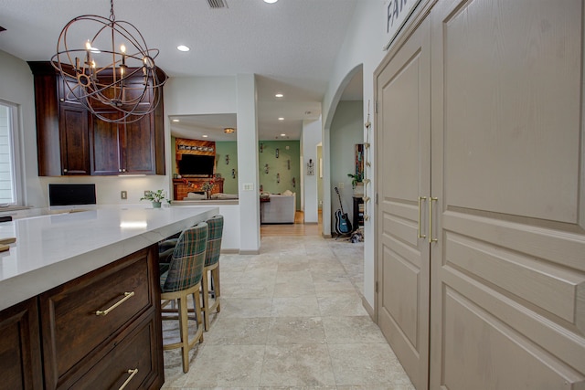 kitchen featuring arched walkways, hanging light fixtures, a textured ceiling, dark brown cabinets, and recessed lighting