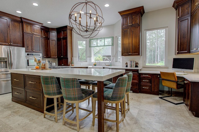 kitchen with built in study area, appliances with stainless steel finishes, light countertops, pendant lighting, and recessed lighting