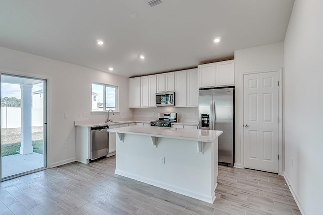 kitchen with stainless steel appliances, light countertops, white cabinets, a kitchen island, and a sink