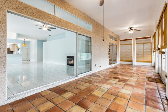 unfurnished sunroom with a tiled fireplace and ceiling fan