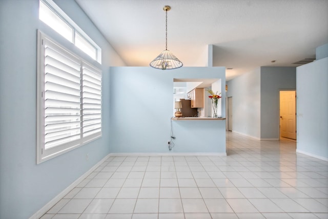 spare room with a chandelier, light tile patterned flooring, and a healthy amount of sunlight