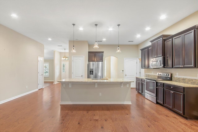 kitchen featuring stainless steel appliances, an island with sink, a kitchen breakfast bar, and decorative light fixtures