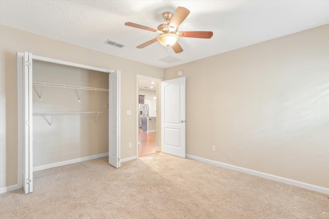 unfurnished bedroom featuring ceiling fan, light colored carpet, a textured ceiling, and a closet