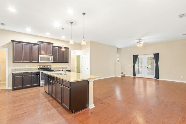 kitchen with pendant lighting, appliances with stainless steel finishes, dark brown cabinetry, a center island with sink, and french doors