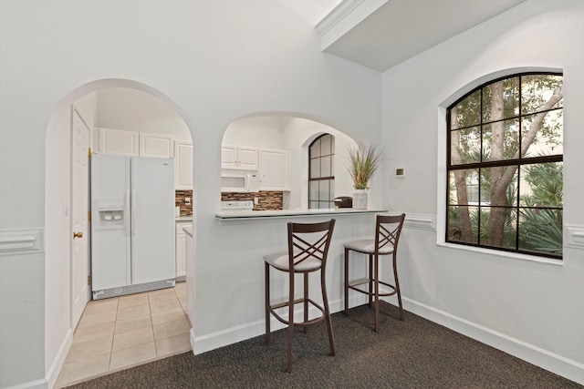 kitchen with white appliances, a breakfast bar, white cabinets, decorative backsplash, and kitchen peninsula