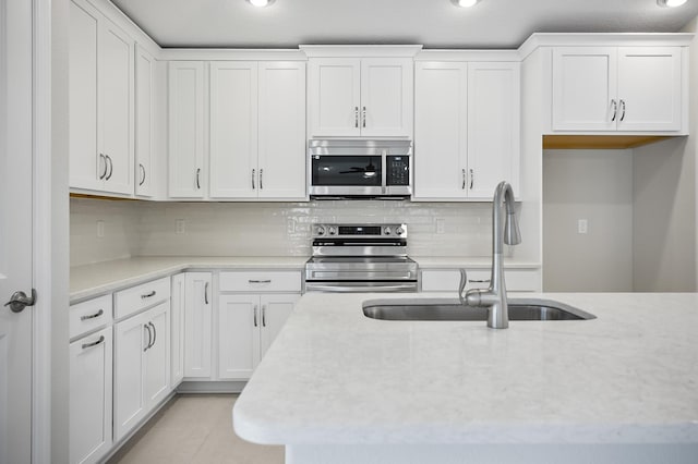 kitchen with light tile patterned flooring, sink, white cabinetry, appliances with stainless steel finishes, and backsplash