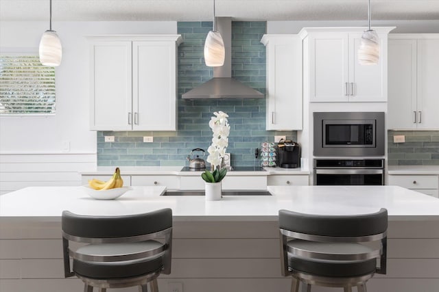 kitchen featuring wall chimney range hood, light countertops, stainless steel appliances, and a breakfast bar
