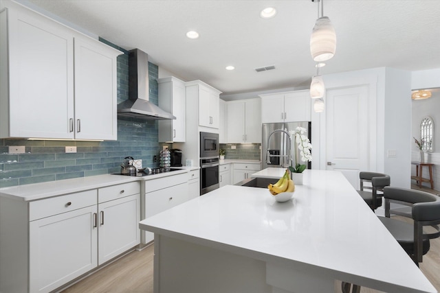 kitchen featuring light countertops, a sink, wall chimney range hood, appliances with stainless steel finishes, and a kitchen island