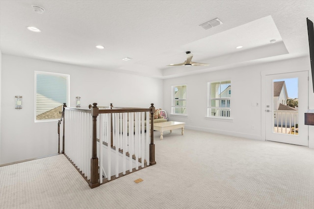 unfurnished room featuring carpet flooring, an upstairs landing, a tray ceiling, visible vents, and ceiling fan