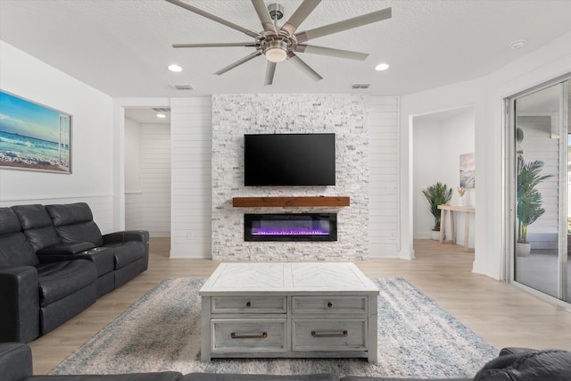living area featuring visible vents, a glass covered fireplace, ceiling fan, and wood finished floors