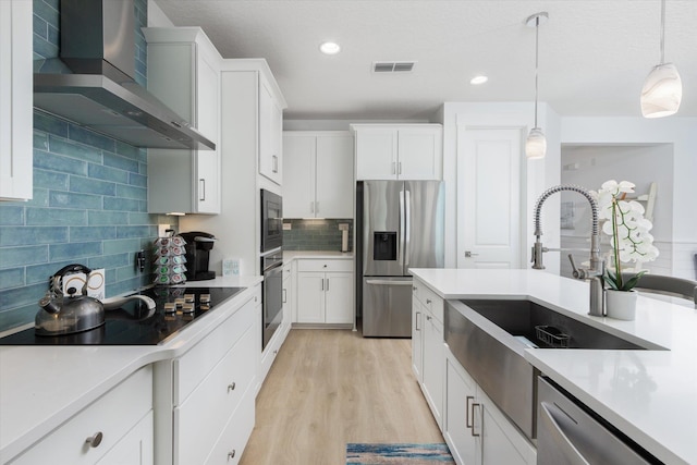 kitchen featuring stainless steel appliances, visible vents, wall chimney exhaust hood, decorative backsplash, and light countertops