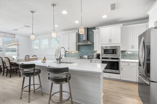 kitchen with stainless steel appliances, a textured ceiling, visible vents, wall chimney exhaust hood, and light countertops