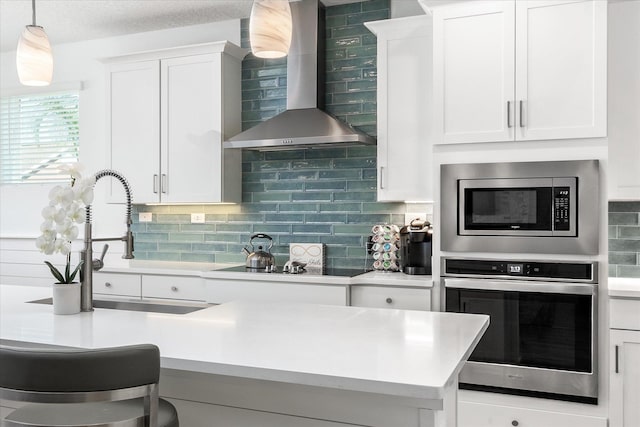 kitchen featuring stainless steel appliances, white cabinets, wall chimney range hood, light countertops, and tasteful backsplash