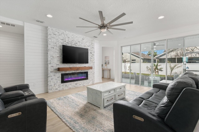 living area featuring a textured ceiling, a ceiling fan, visible vents, and light wood-style floors