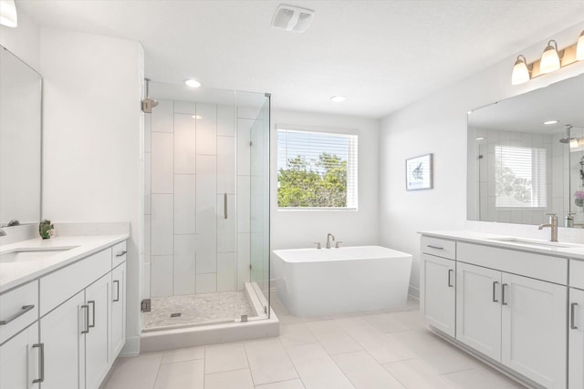 bathroom featuring a stall shower, a freestanding tub, two vanities, and a sink