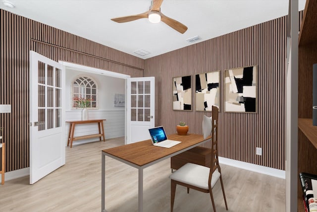 home office with light wood-style flooring, a ceiling fan, visible vents, and wood walls