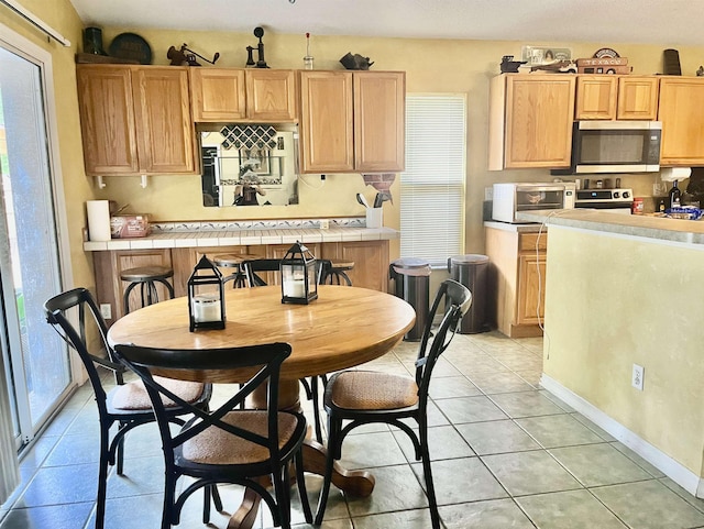 kitchen with tile countertops, light tile patterned floors, light brown cabinetry, and appliances with stainless steel finishes