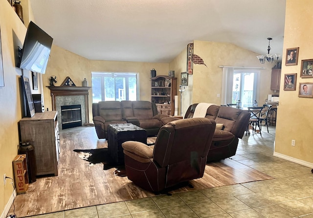 living room featuring a notable chandelier, light hardwood / wood-style floors, a fireplace, and vaulted ceiling