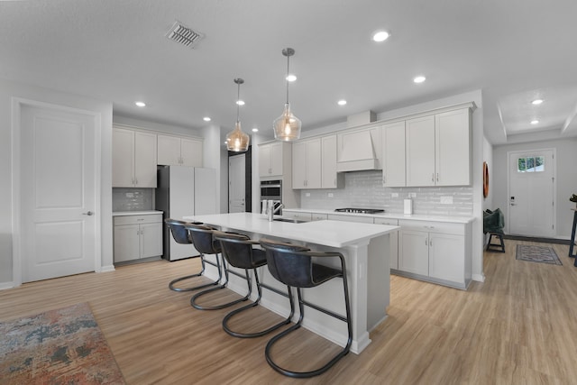 kitchen featuring gas stovetop, visible vents, light countertops, custom exhaust hood, and freestanding refrigerator