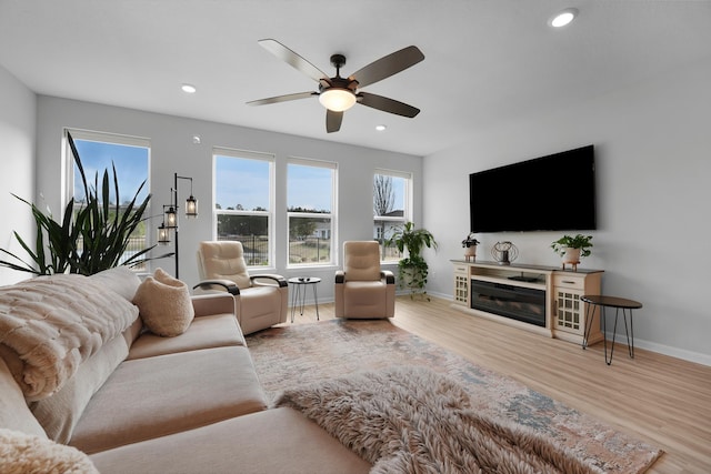 living area featuring wood finished floors, ceiling fan, plenty of natural light, and baseboards