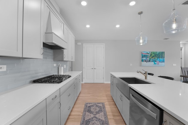 kitchen with a sink, stainless steel appliances, tasteful backsplash, custom exhaust hood, and light countertops
